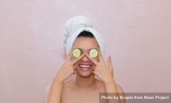 Young woman covering her eyes with cucumber 0go330