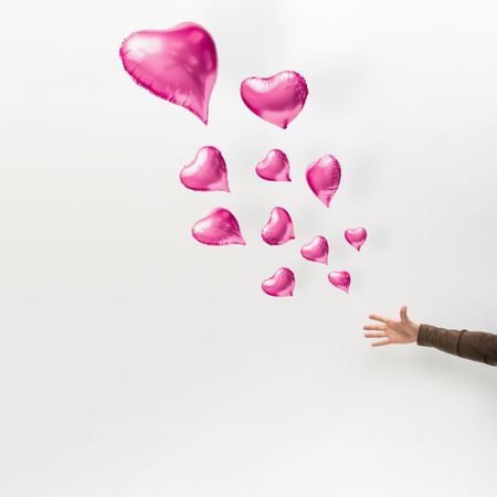 Hand releasing pink heart balloons on light background