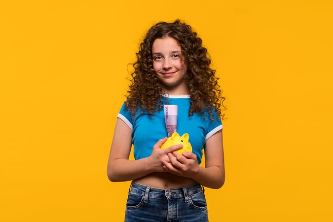 Girl holding piggy bank and smiling, demonstrating financial savings