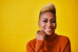 Studio shot of joyful Black woman with short blonde hair in orange sweater