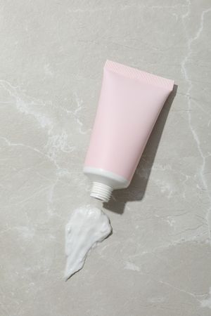 Pink tube with cream on gray background, top view