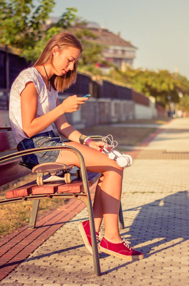 Young girl with skateboard and headphones looking smartphone