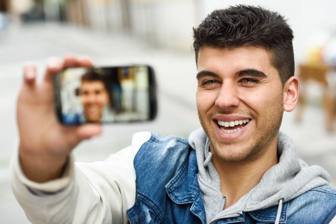 Smiling man in jean jacket taking selfie outside