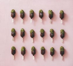 Rows of ice cream chocolate pistachio popsicles, pink background