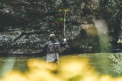 Confident man fishing with rod while standing in river stream