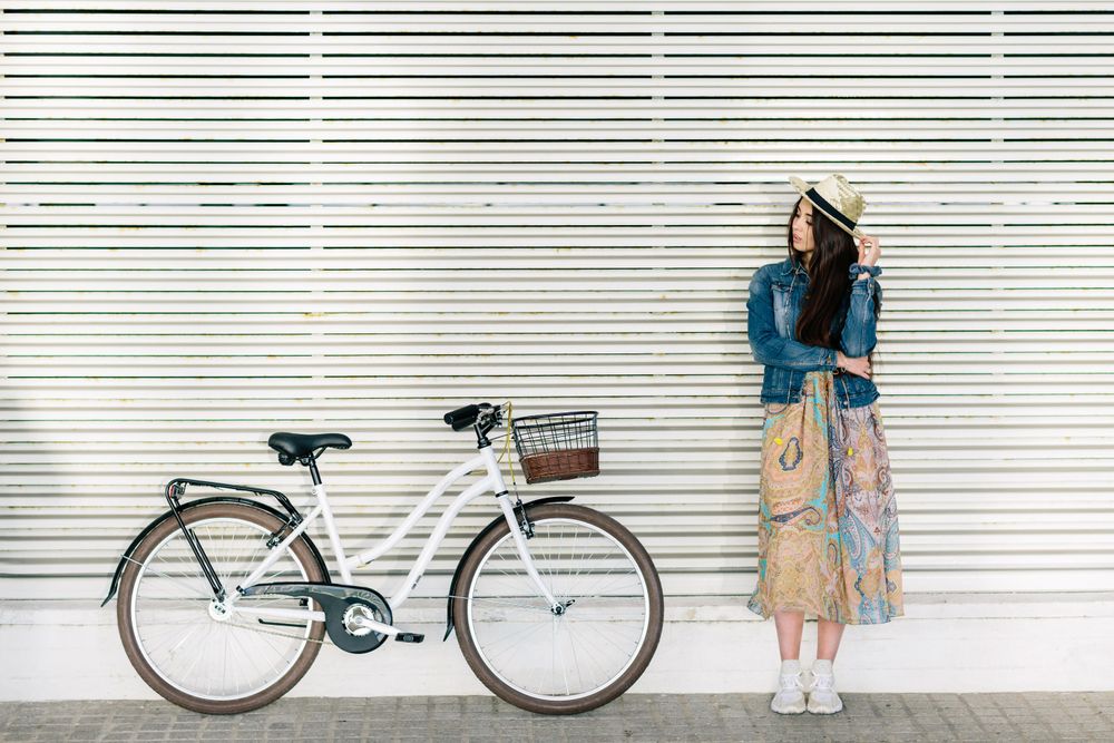 Woman in floral dress leaning on light wall beside light bicycle