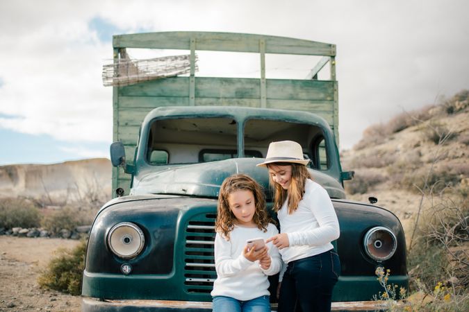 Cheerful girls watching smartphone near abandoned truck