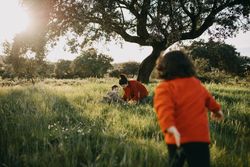 A young girl walks towards her mother and brother in a field