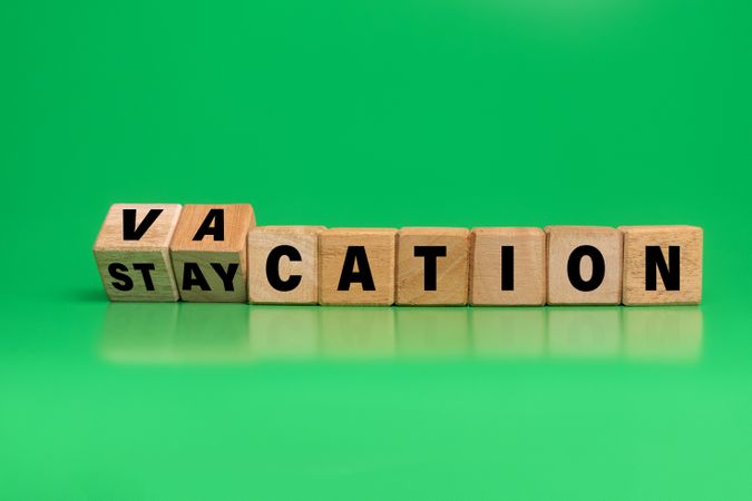 turned wooden blocks with vacation and staycation words symbol isolated on green background