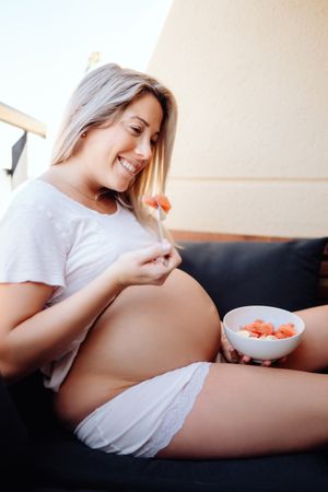 Faceless pregnant woman eating fruits with fork