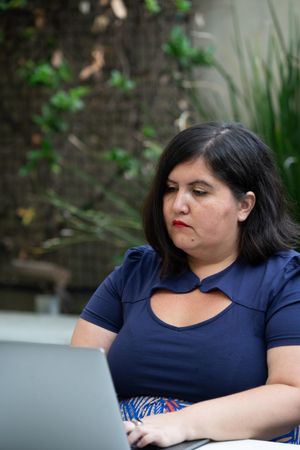 Woman using laptop outside with plants in the background