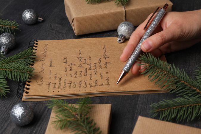 Notepad with text, pen in hand and gift boxes on wooden background