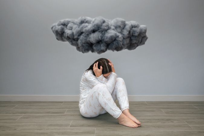 Unrecognizable woman crying under cloud holding her head