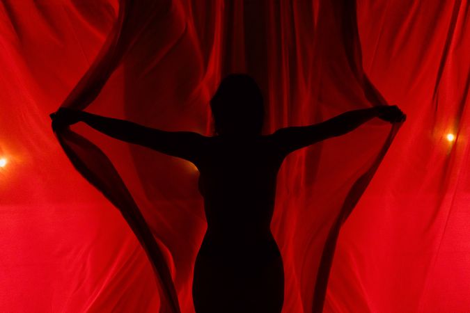 Anonymous enigmatic woman opening red curtains
