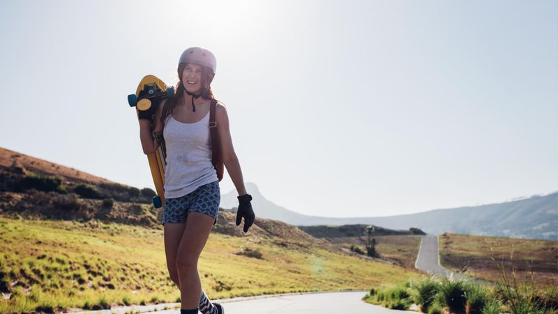 Happy young woman walking with a longboard on countryside road