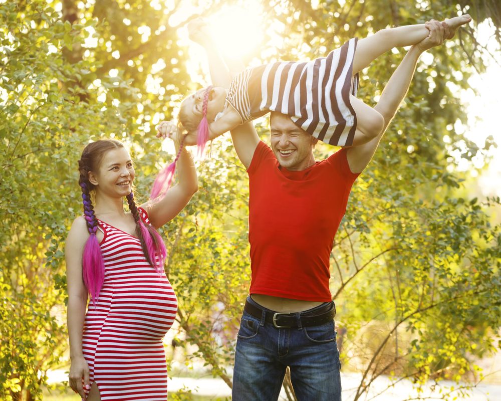 Father lifting daughter above his head in sunny park under trees