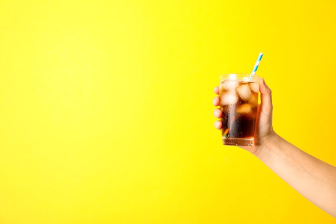 Female hand holding a glass with ice cola and tubule