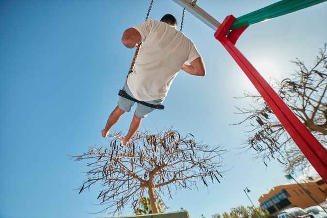 Man swinging on playground in sunlight