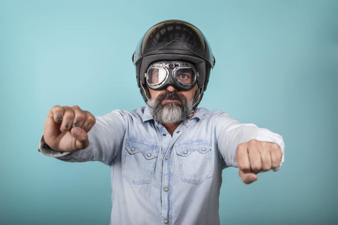 Portrait of man with helmet and glasses pretending to ride a motorcycle in studio