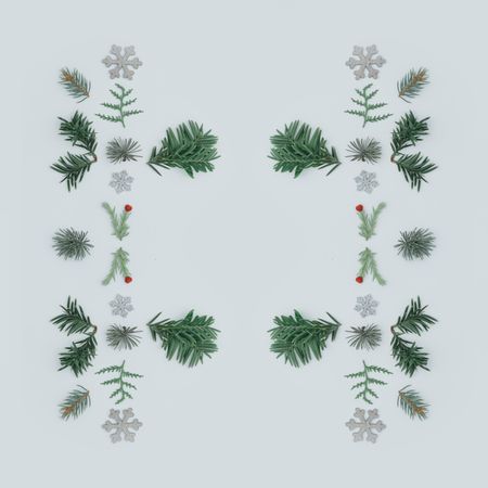 Symmetrical layout made with tree branches and red berries on grey background with snowflakes