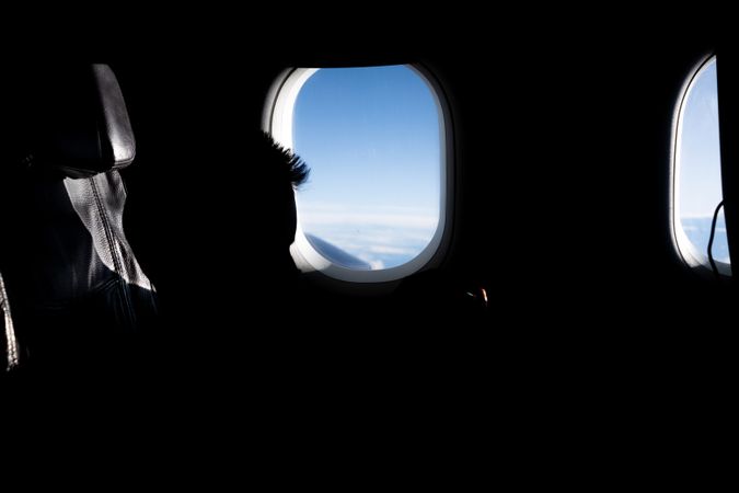 Window showing bright blue sky in dark airplane