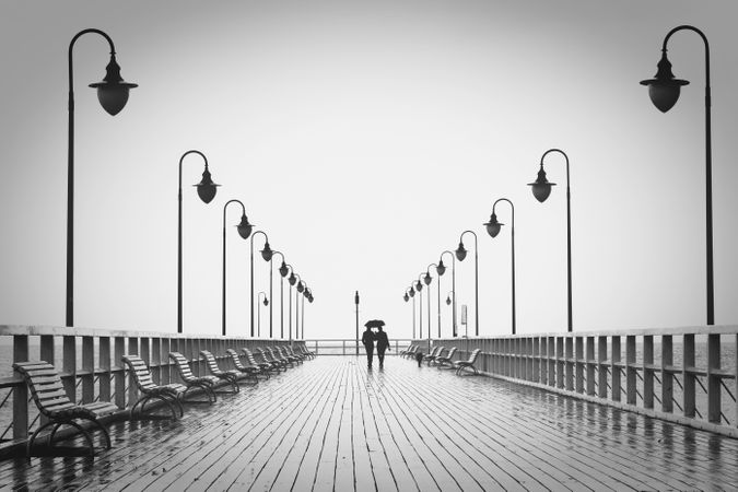 Silhouette of two people walking on bridge under umbrella