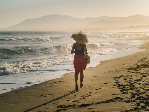 Woman in hat and running along seaside