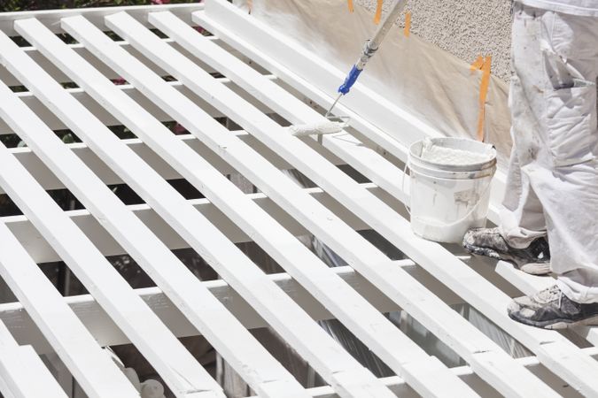 Painter Rolling White Paint Onto Top of Patio Cover