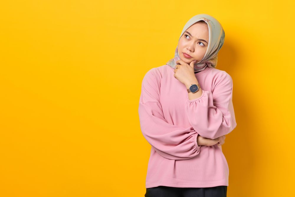 Muslim woman in headscarf in deep thought with head tilted and hand on chin