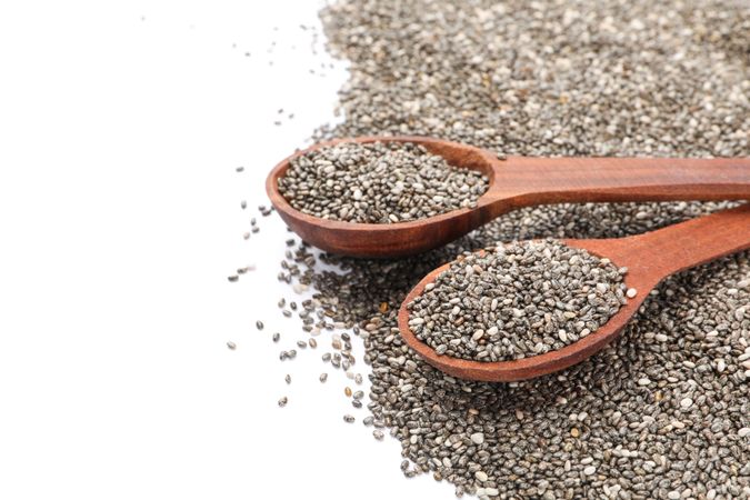 Chia seeds and wooden spoons isolated on plain background