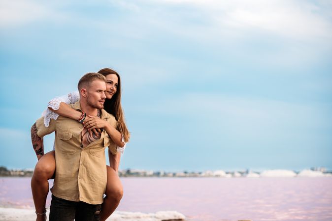 adorable couple giving a piggyback ride on an amazing beach of pink water