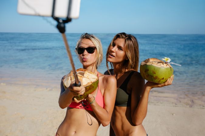 Female friends on beach with coconuts taking selfie