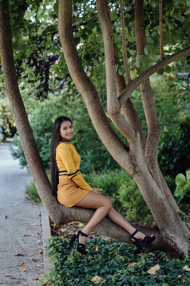 long haired Asian woman sitting on trunk of tree