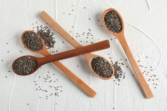 Wooden spoons and chia on plain background, top view