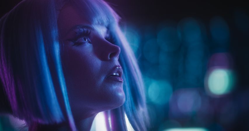 Cinematic Close Up Portrait of a Young Cosplay Model Wearing Futuristic Clothes, Striking Makeup and a Short Blue Wig, Female Enjoying a Beautiful Night Life Scenery in a Neon High Tech City
