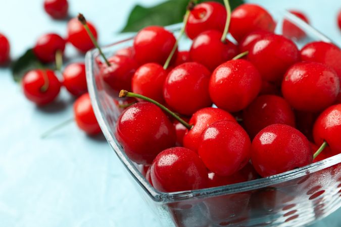 Bowl with red cherry on blue background, close up