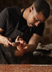 Black baker sifting chocolate onto dessert in professional kitchen