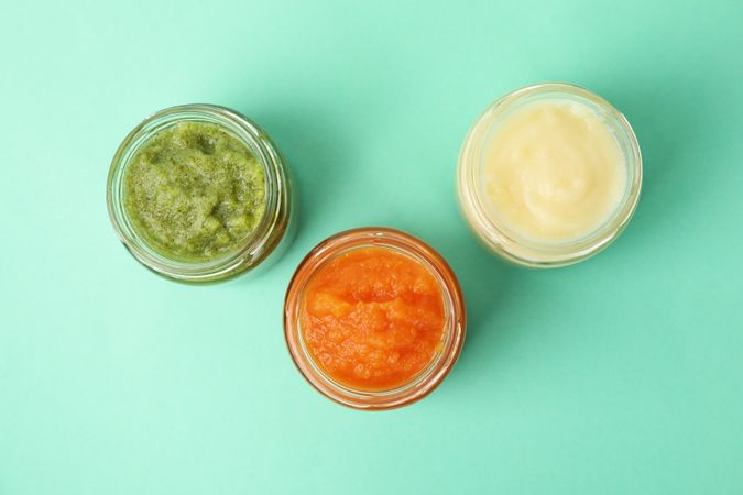 Glass jars with vegetable puree on mint background. Baby food