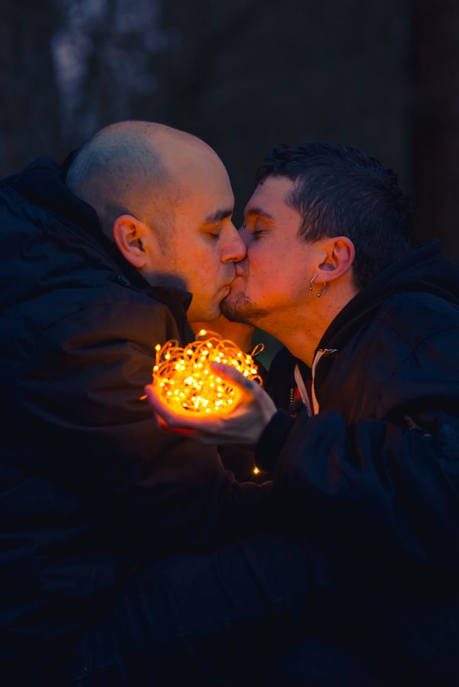 Men kissing and holding fairy lights near dog in forest at night