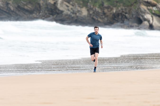Sportsman in active wear jogging on lonely beach