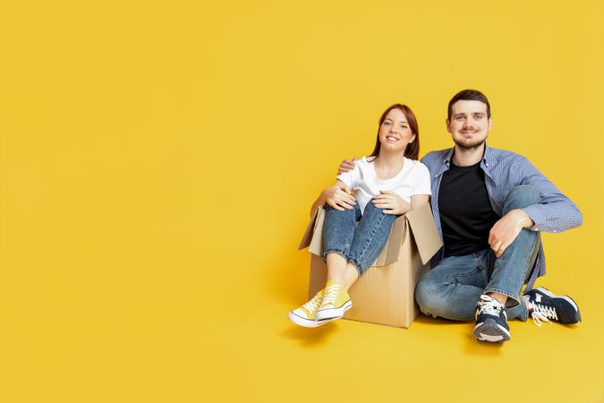 A couple with boxes, on a yellow background, the concept of moving.