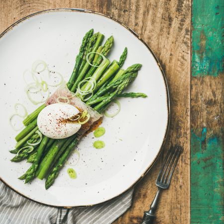 Asparagus and soft boiled egg on plate, on wooden table with green trim, square crop