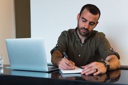 Man writing in notebook near laptop