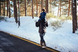 Man with kid on neck walking on road along snowy forest
