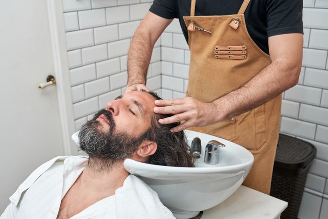Crop barber washing hair of client in salon