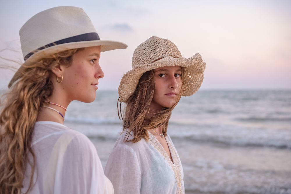 Smiling girlfriends in summer clothes barefoot in water on beach