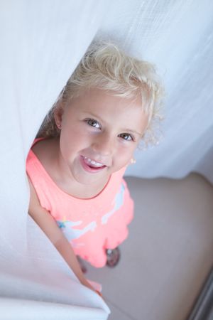 Smiling little girl standing near curtain at home