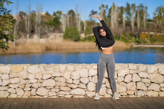 a young female athlete stretches on a rock wall next to a lake