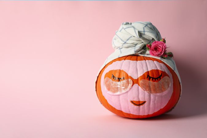 Pumpkin with eye patches and towel on pink background