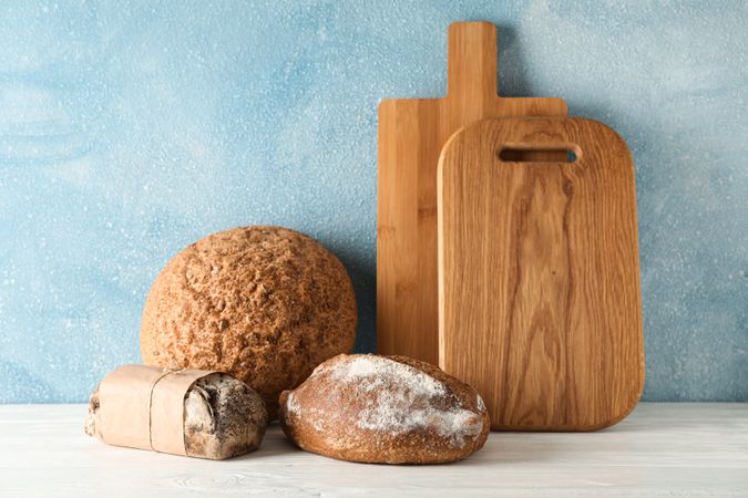 Bakery products and cutting boards on wooden table against light background, space for text